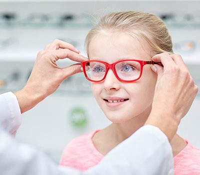 Eine Optikerin setzt einem Mädchen eine Kinderbrille auf.